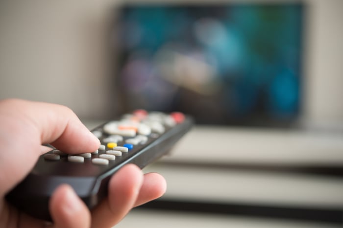 Close-up shot of hand holding TV remote, with a blurred screen in the distance.