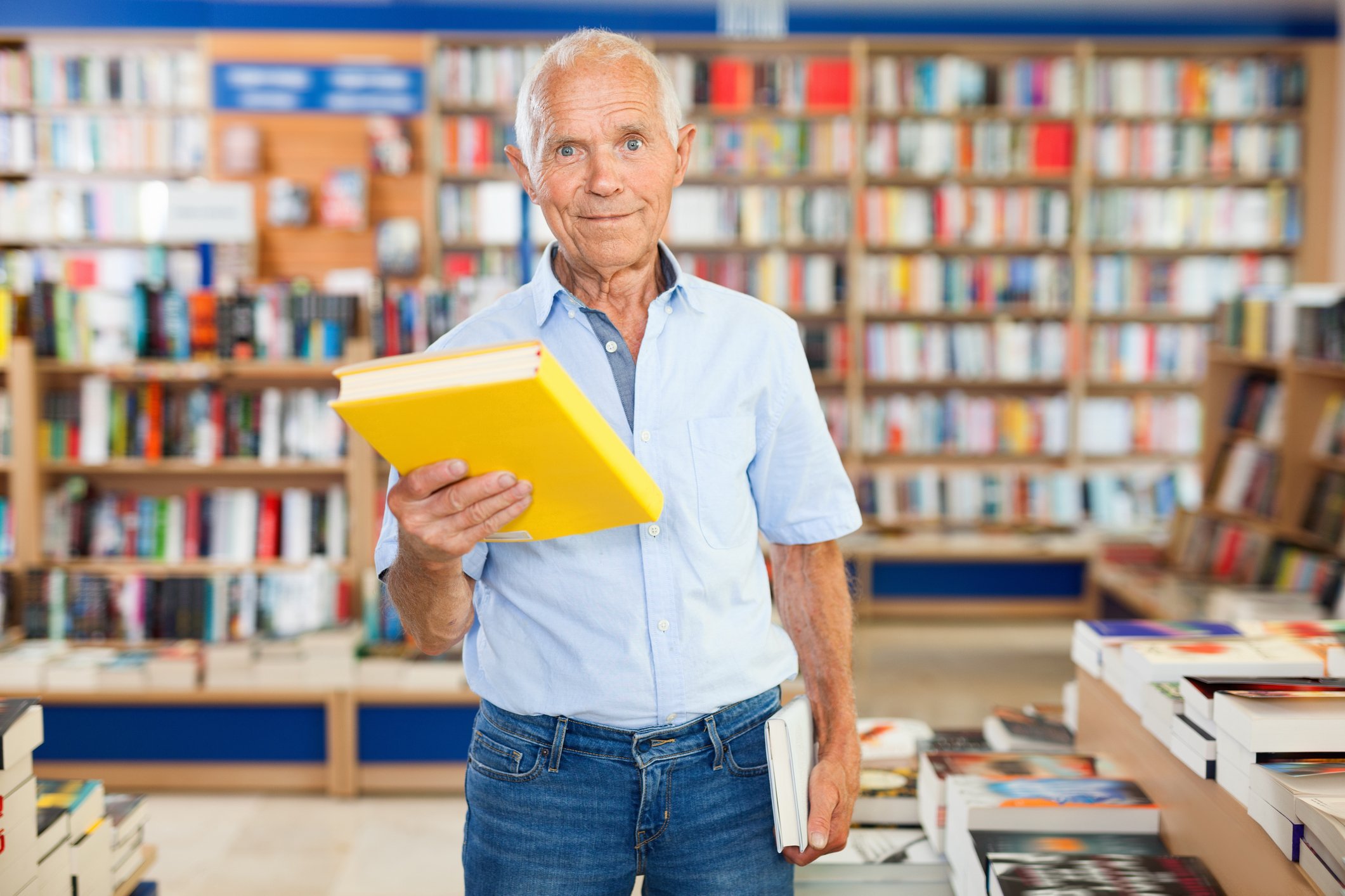 An older man holds up a book in a bookstore
