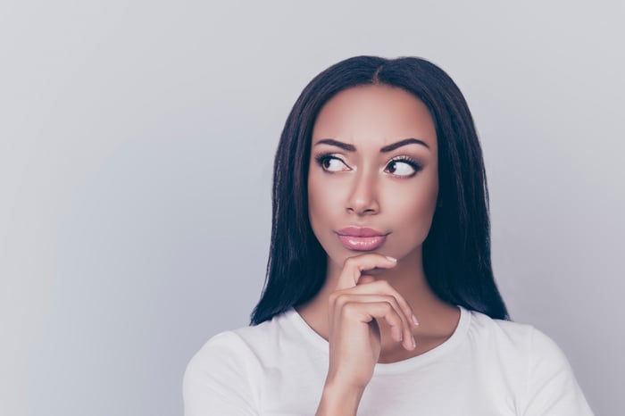 A woman looks off to the side and has a hand to her chin, as if she's thinking.