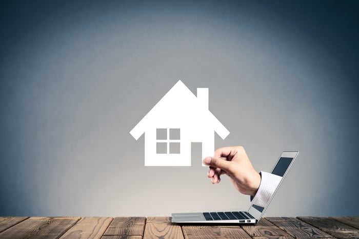 A hand emerging from a laptop holding a house.