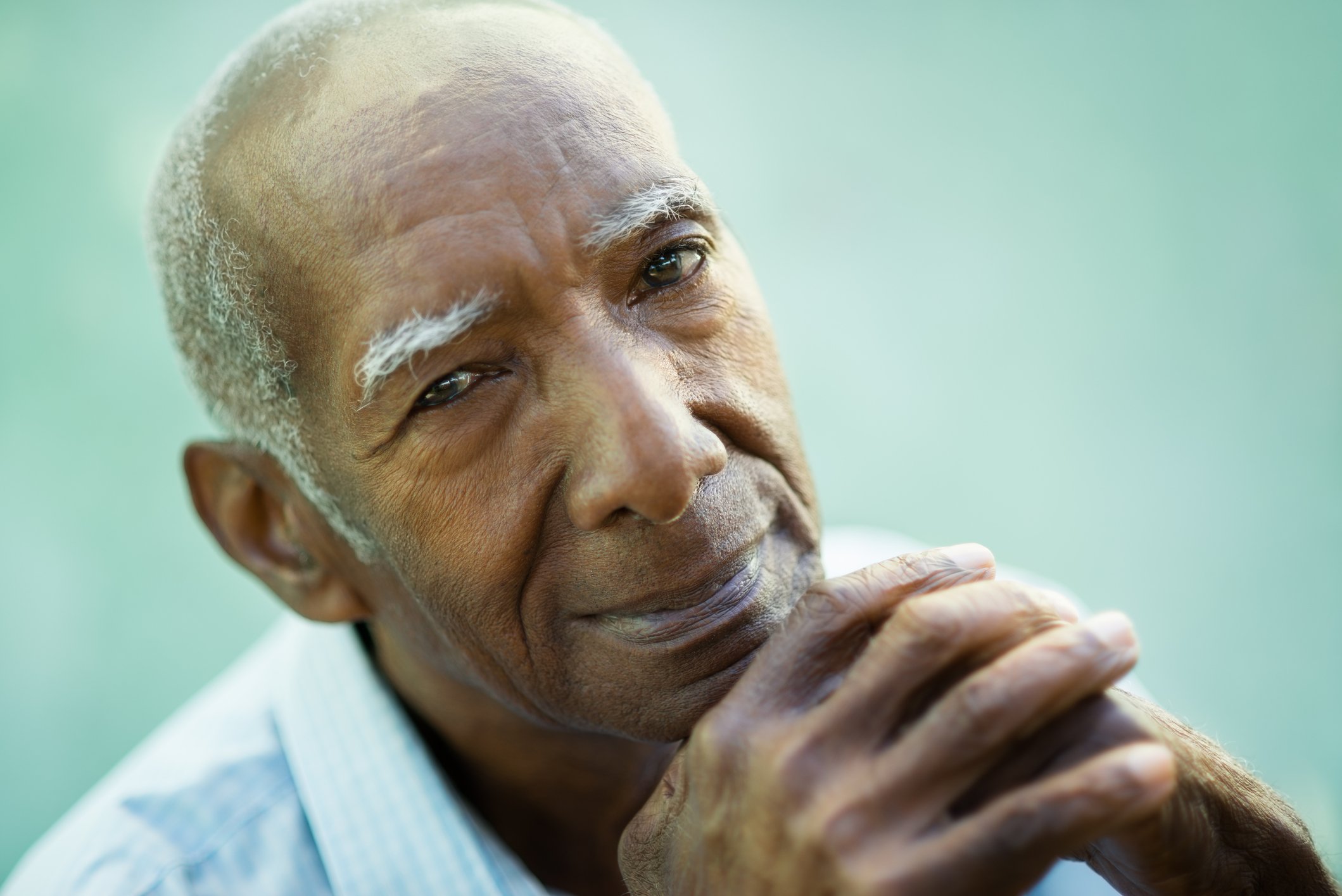 A senior man in deep thought, with his hands interlocked in front of his chin. 
