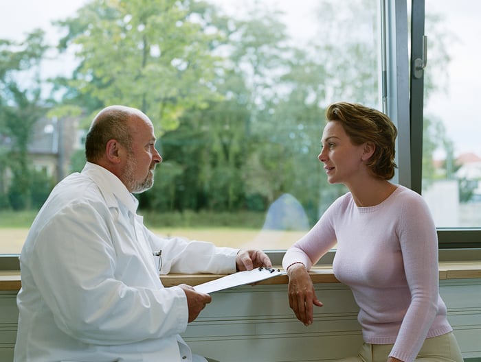 A male doctor sitting and talking to female patient in front of a window