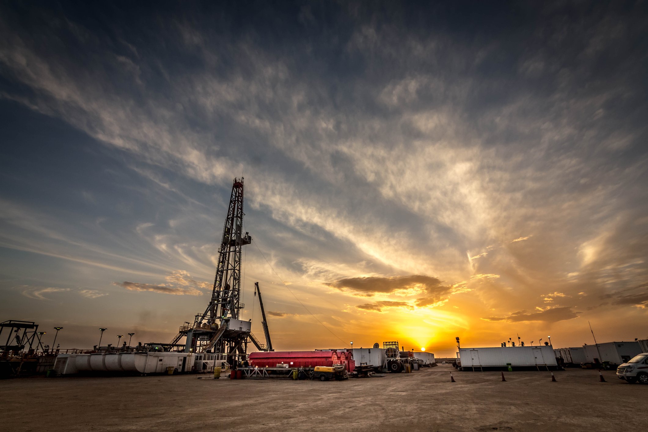 A drilling rig site with the sun setting in the background.
