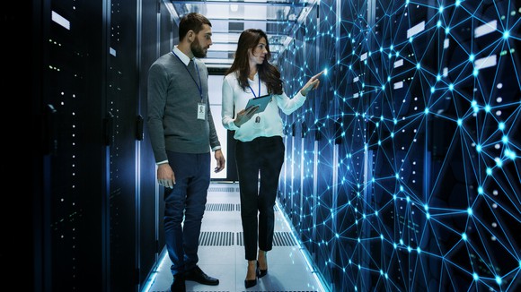 Female and Male IT Engineers Discussing Technical Details in a Working Data Center/ Server Room with Internet Connection Visualization.