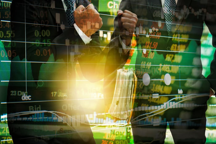 Two men in suits shown behind a stock board.