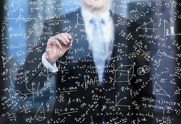 A man in a suit does financial calculations on a glass wall in the foreground.