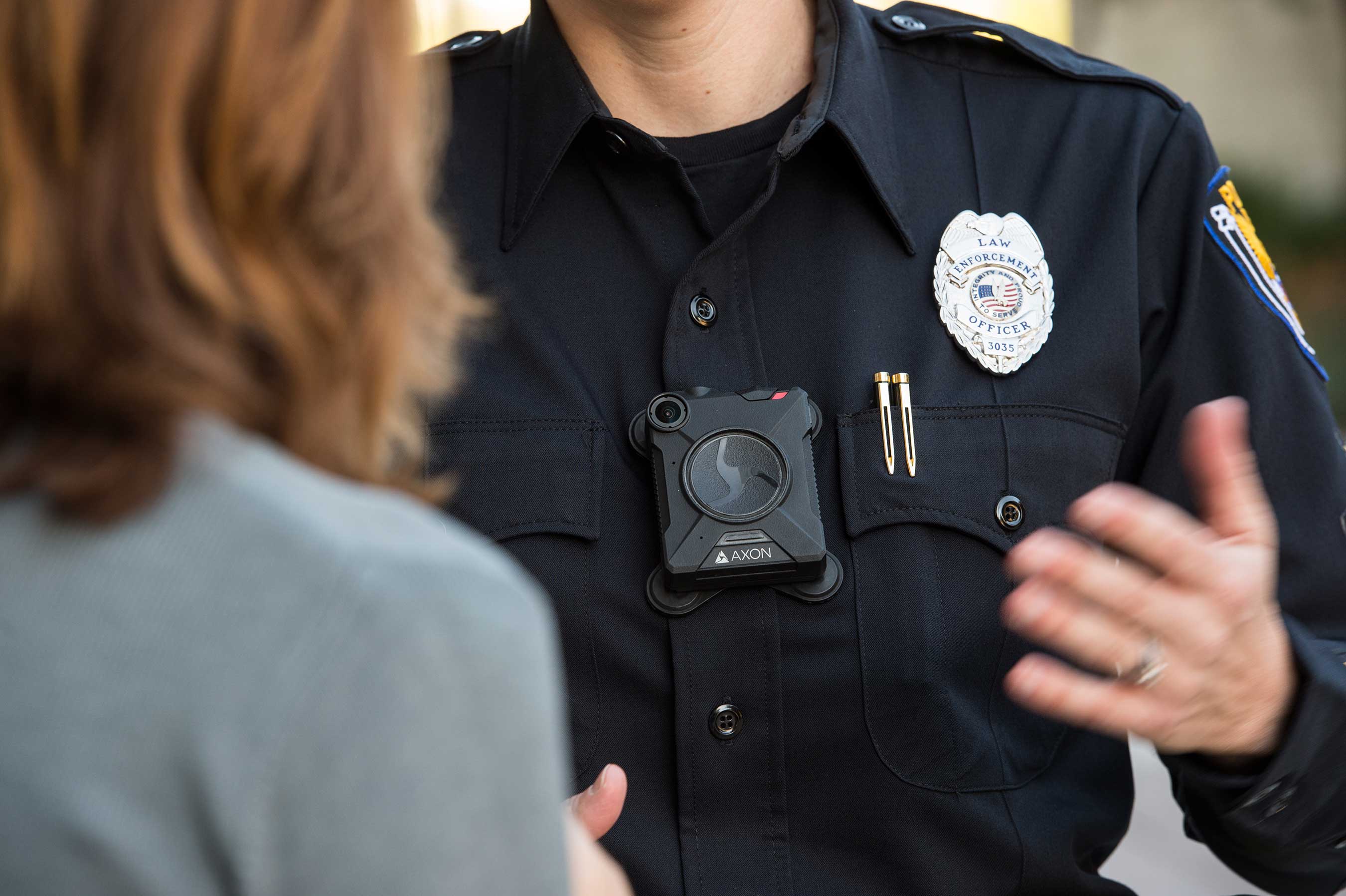 Law enforcement officer wearing a body camera on his chest, talking with another person.