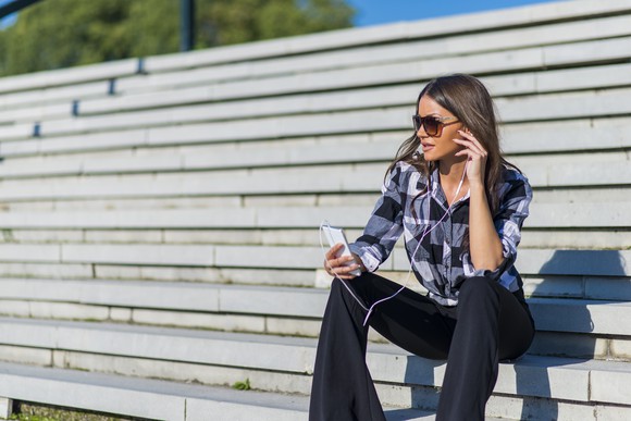 Lady listening to headphones plugged into a smartphone.