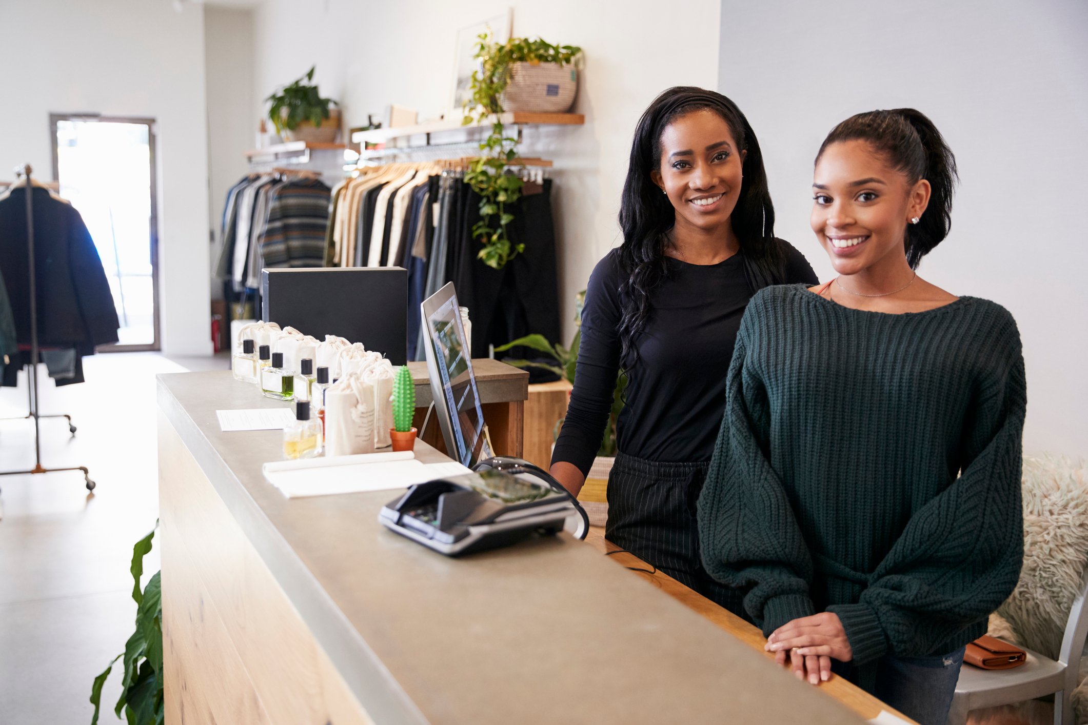 Two women are behind a counter at a clothing store.