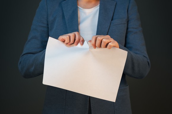 A person in a sportcoat is tearing a piece of paper.