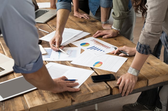 Several people review financial documents spread across a table.