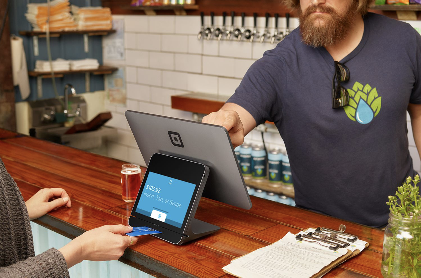 A woman using her credit card to checkout with a Square payment system in a store.