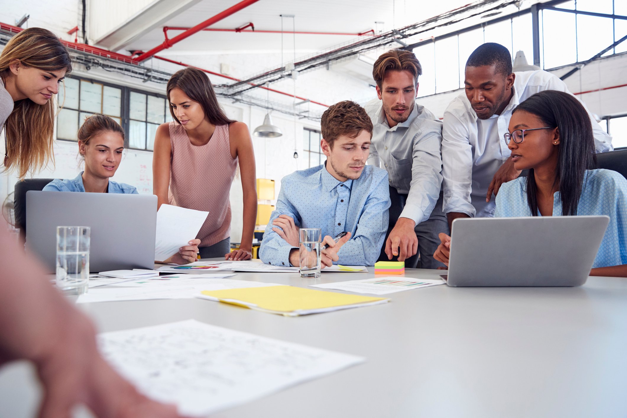 Younger workers in an office gathered around laptops and looking at papers on a table