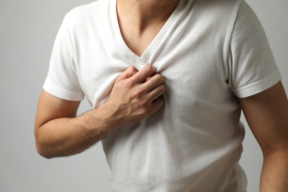 Man in a white v-neck shirt clutching his chest