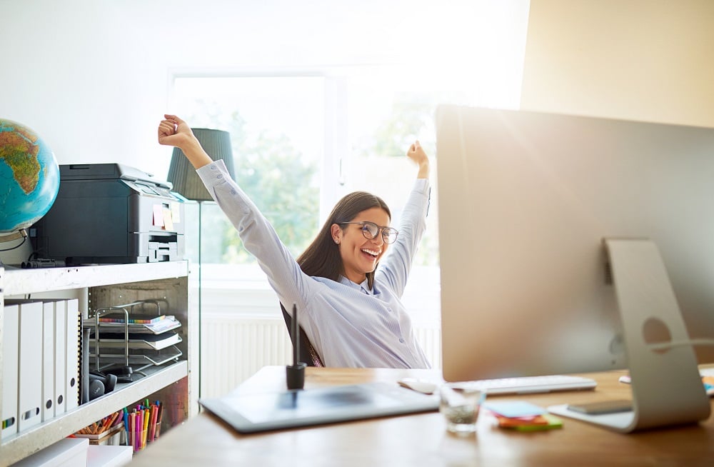 Woman smiling and raising her hands from behind a desk.