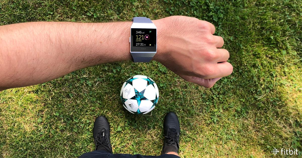 Man wearing a Fitbit device and standing over a soccer ball.