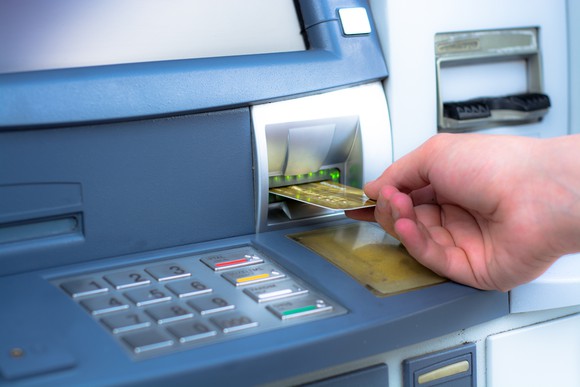 A person is pulling a debit card out of an ATM.