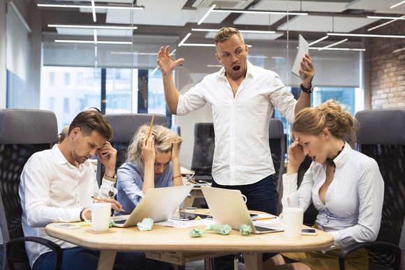 Man yelling at three professionals seated at a table