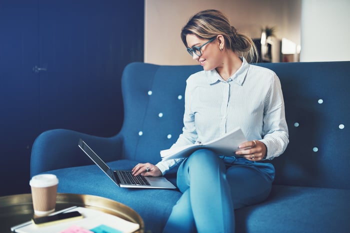 A woman types on a laptop sitting on a couch. 