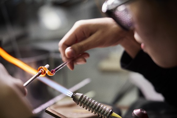 A Thai worker shapes a glass charm over a flame.