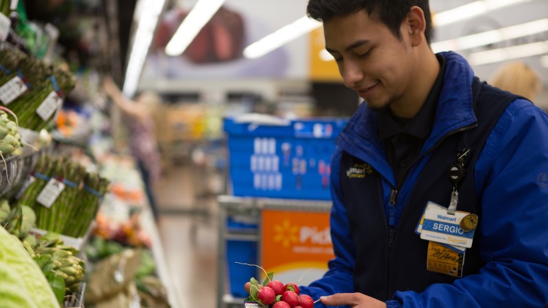 A Walmart employee placing vegetables on display.