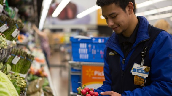 A Walmart employee placing vegetables on display.
