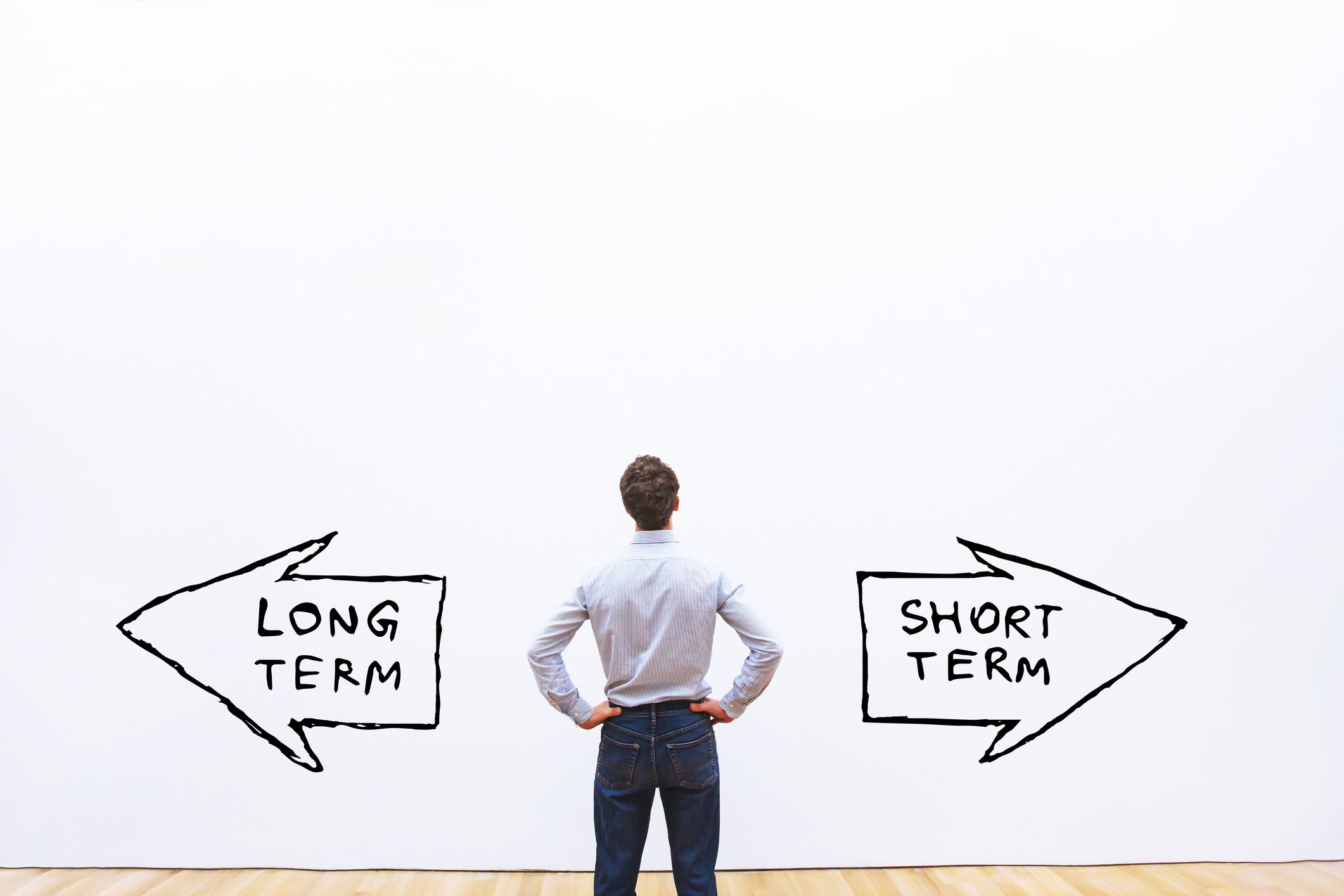 Man looking at a white wall with two arrows pointing in opposite directions. One says short term, the other says long term