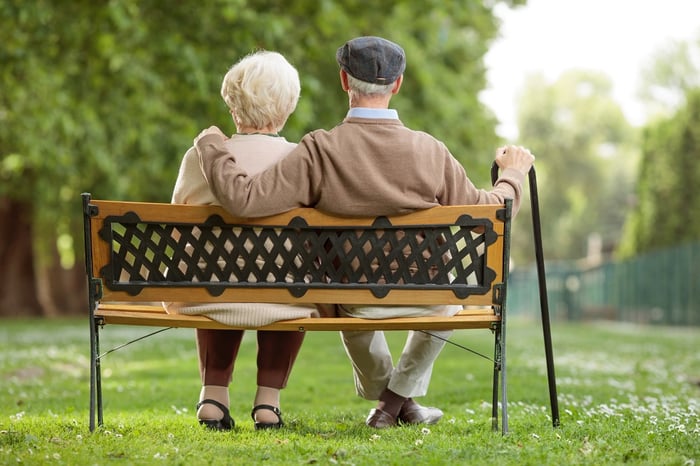 An older man and woman sitting on a park bench.