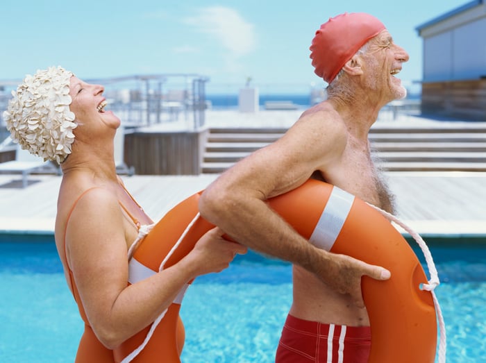 Two seniors laugh while carrying a life preserver.