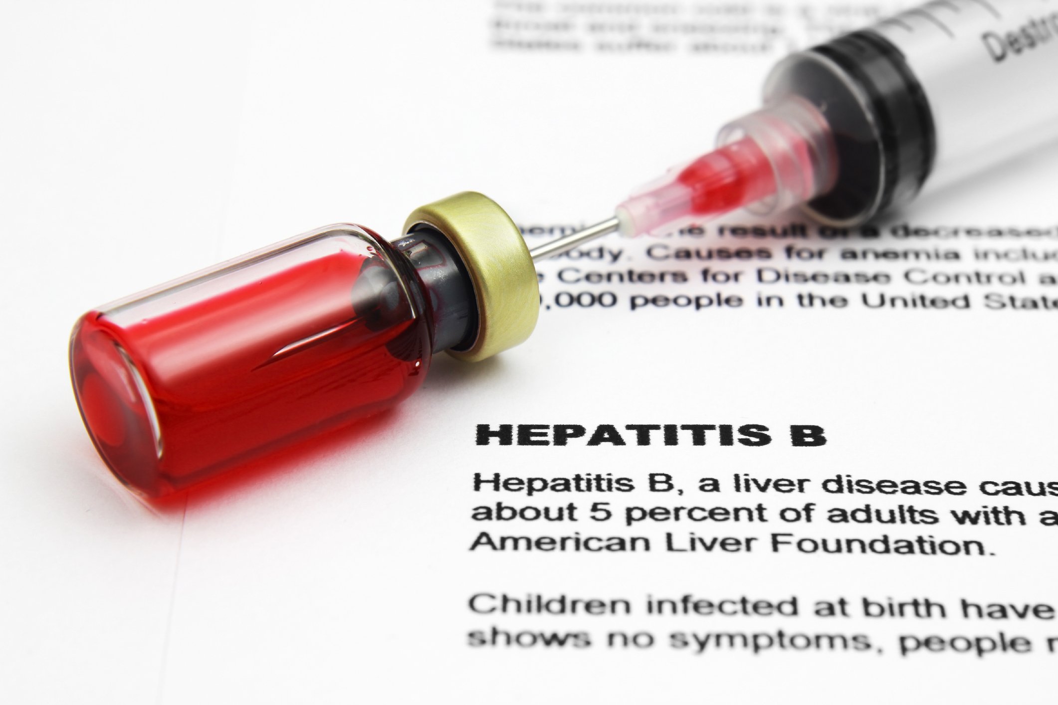 Syringe with vaccine bottle on top of document with information about hepatitis B