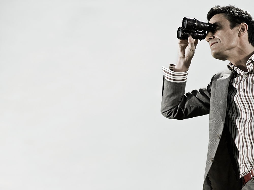Man in a blazer looking through binoculars.