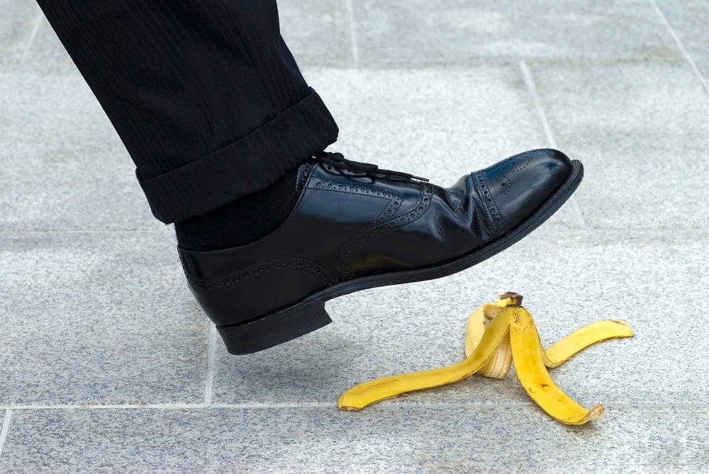 A black shoe about to step on a banana peel.