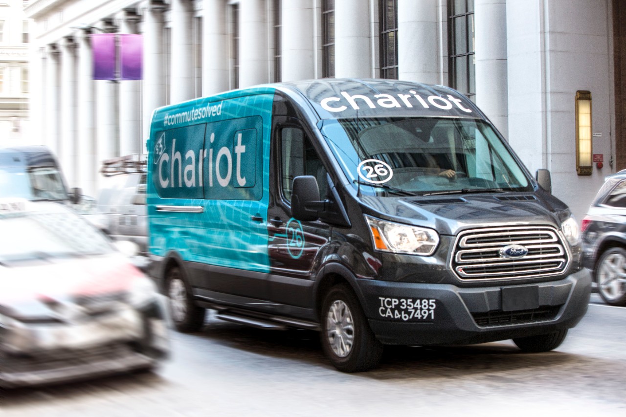 A Ford Chariot branded van driving downtown.
