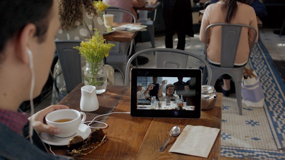 A person streaming Netflix on a tablet in a cafe.
