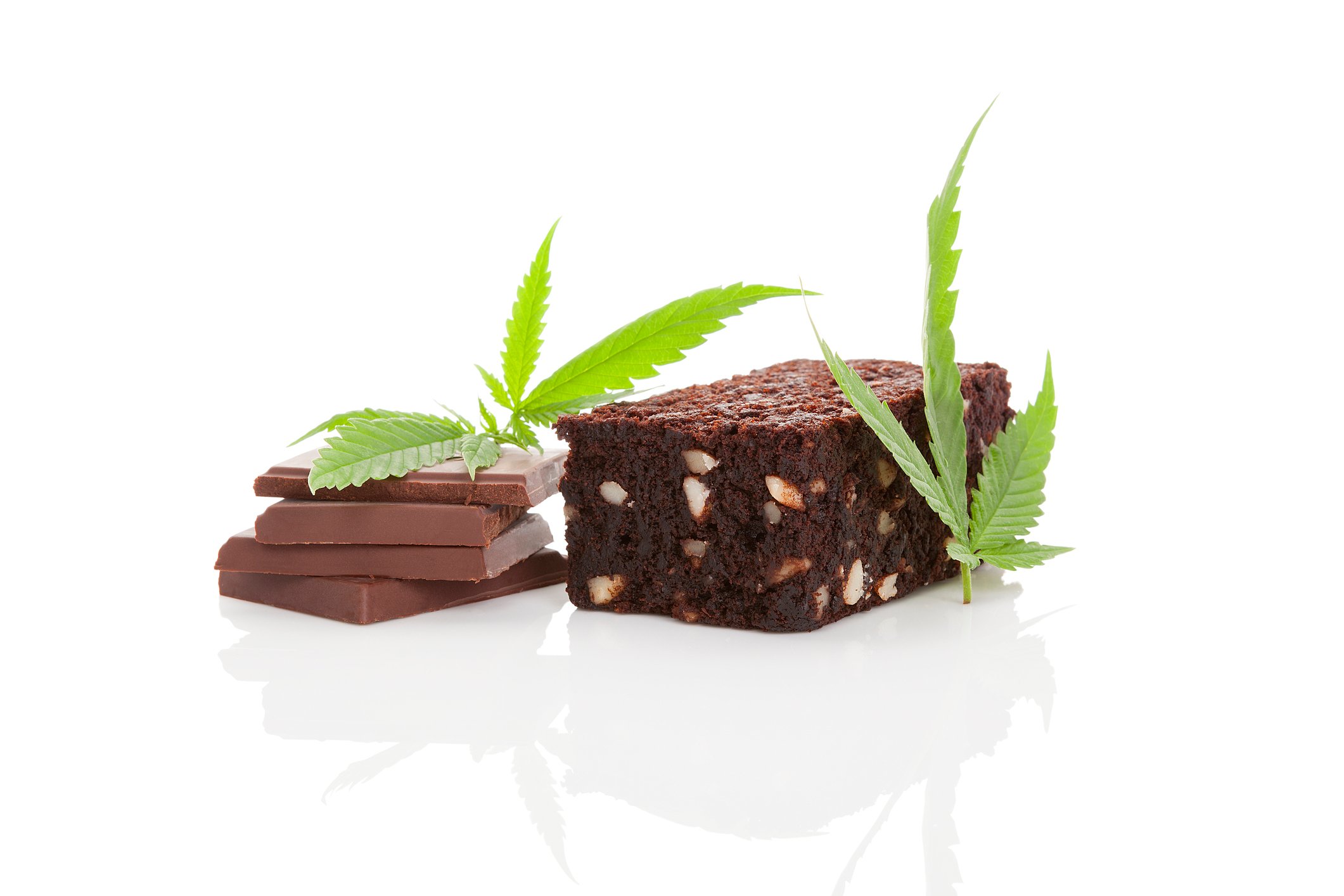 Cannabis leaves next to a chocolate brownie and stacked pieces of chocolate. 