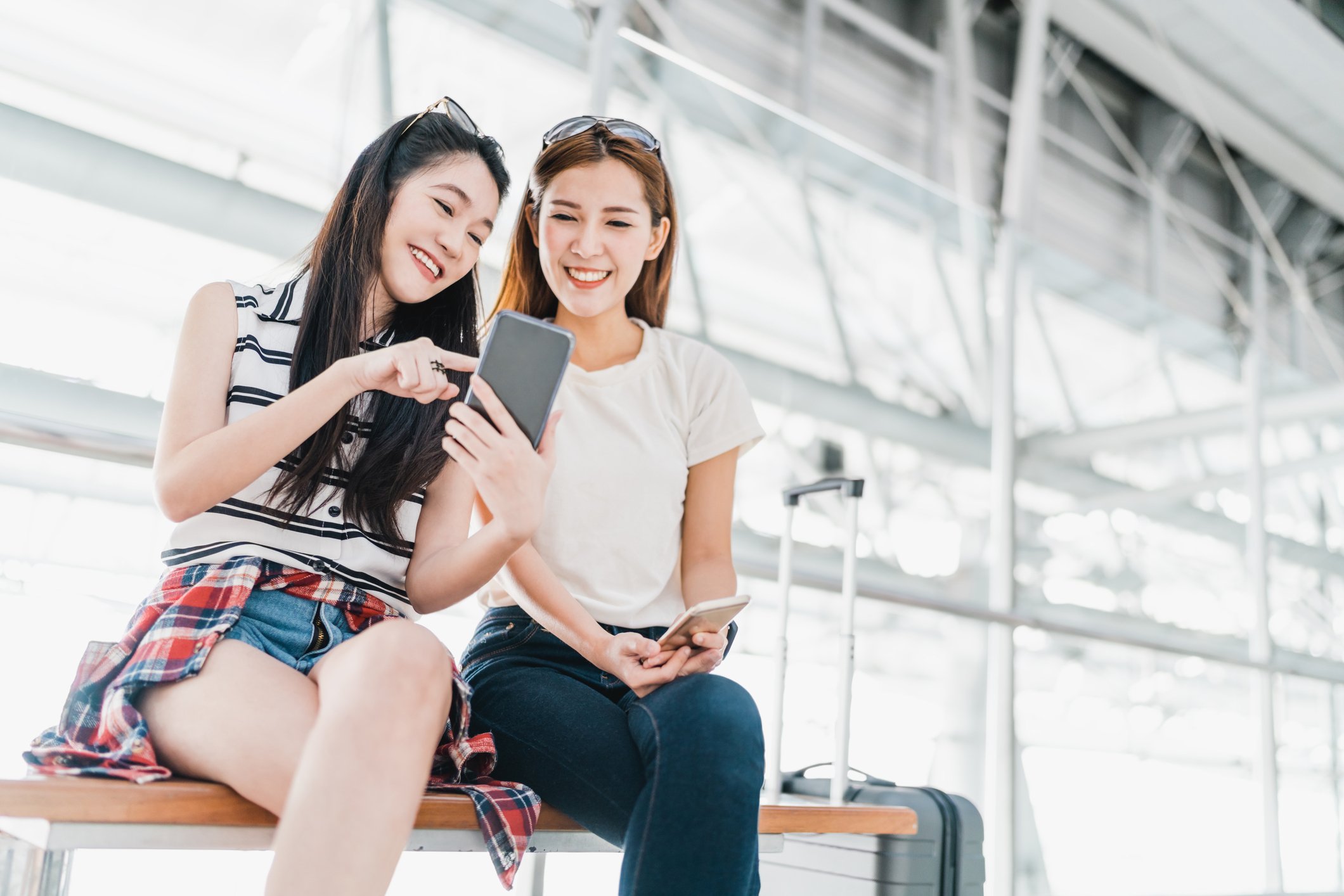 Two smiling young Chinese women pointing at a smartphone screen.