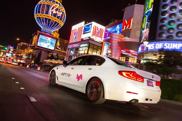 A white BMW with Aptiv and Lyft logos is shown on a Las Vegas street at night.