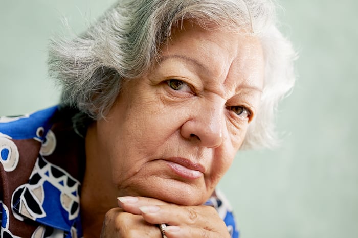 A senior woman in deep thought with her chin resting on her interlocked hands. 