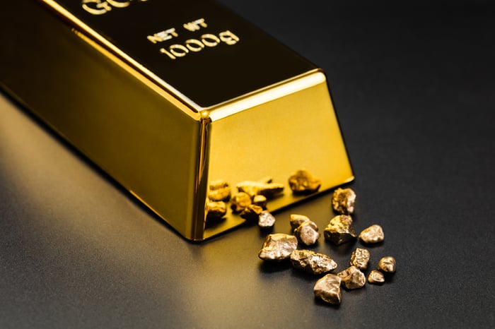 A polished gold bullion with tiny gold fragments next to it.