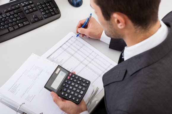 Man in suit using a calculator while reviewing a ledger.