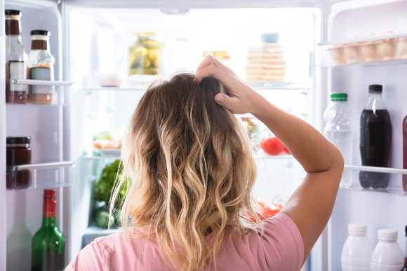 Rear view of a woman scratching her head while looking in open refrigerator