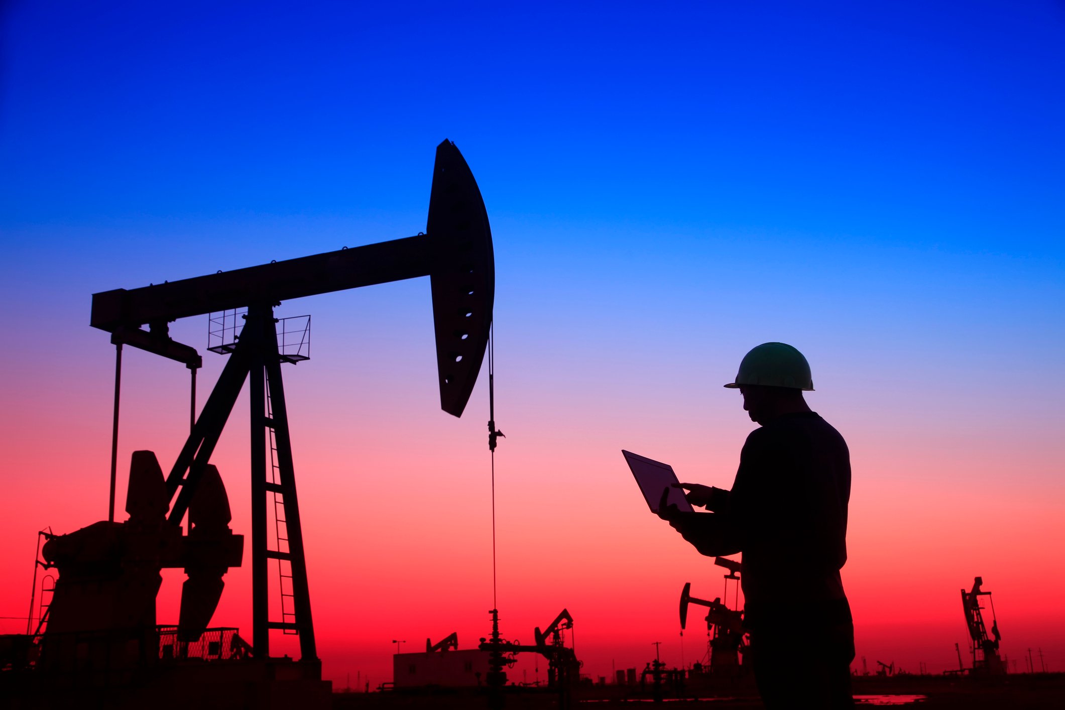 Rows of oil pumps under a twilight sky, with an oil worker in the foreground.