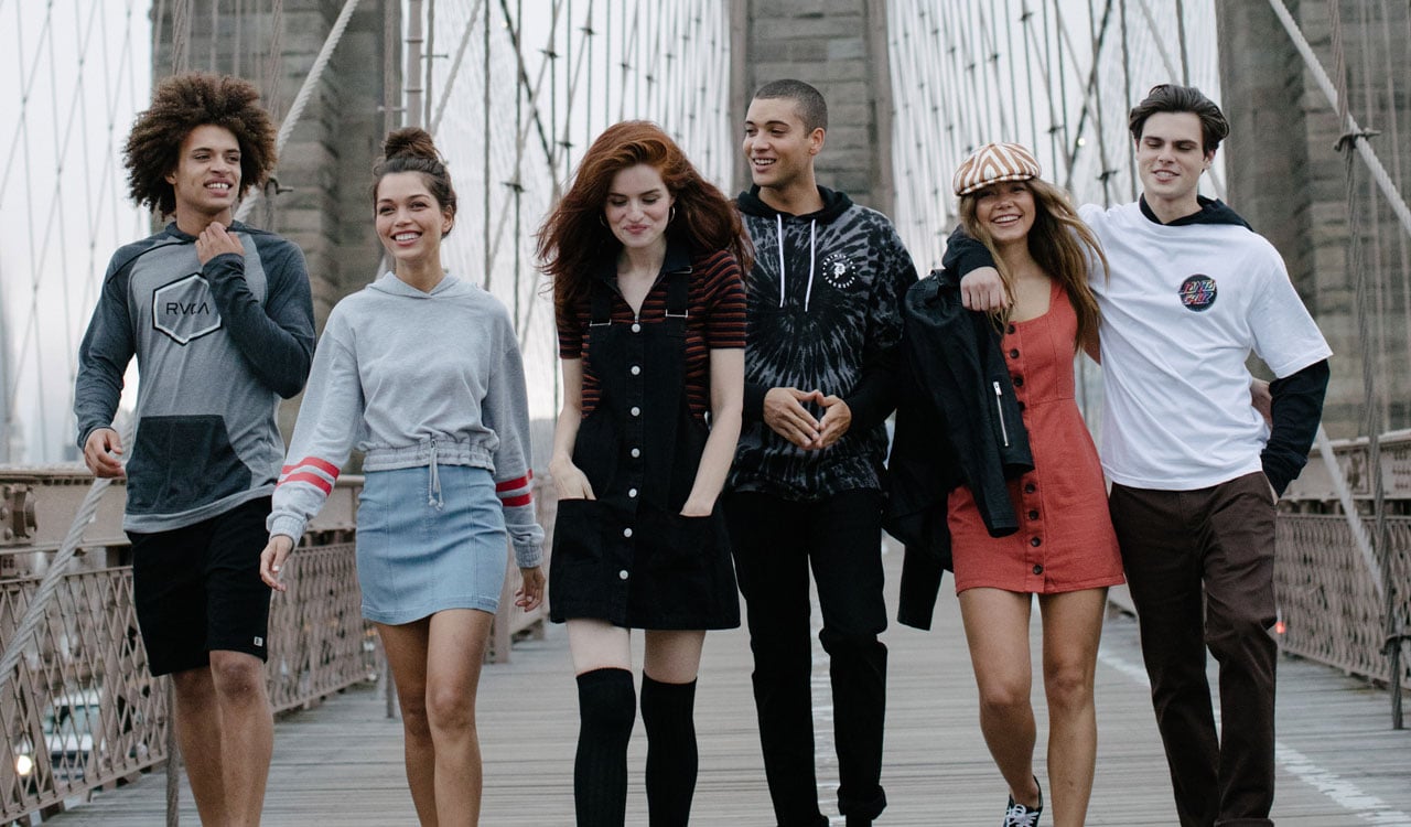 A group of young people walking on a bridge and wearing Tilly's clothing.