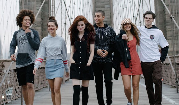 A group of young people walking on a bridge and wearing Tilly's clothing.