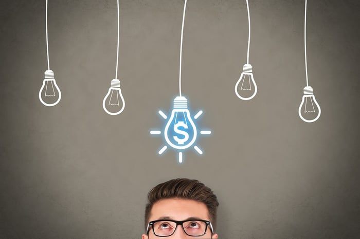 Man looks up at a row of five lightbulbs on chalkboard. The middle lightbulb has a blue dollar sign inside.