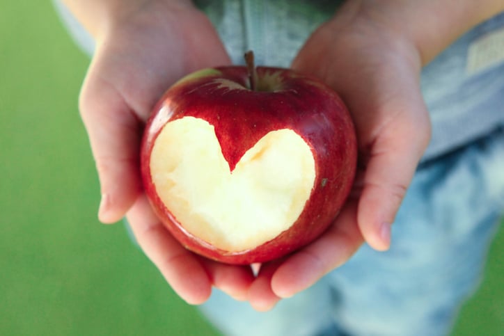 Someone holding an apple with a heart shape cut out of it.