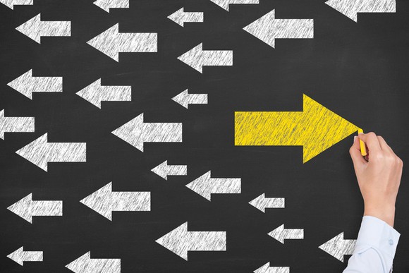 A single yellow arrow pointed in one direction, with many white arrows pointing in the opposite direction.