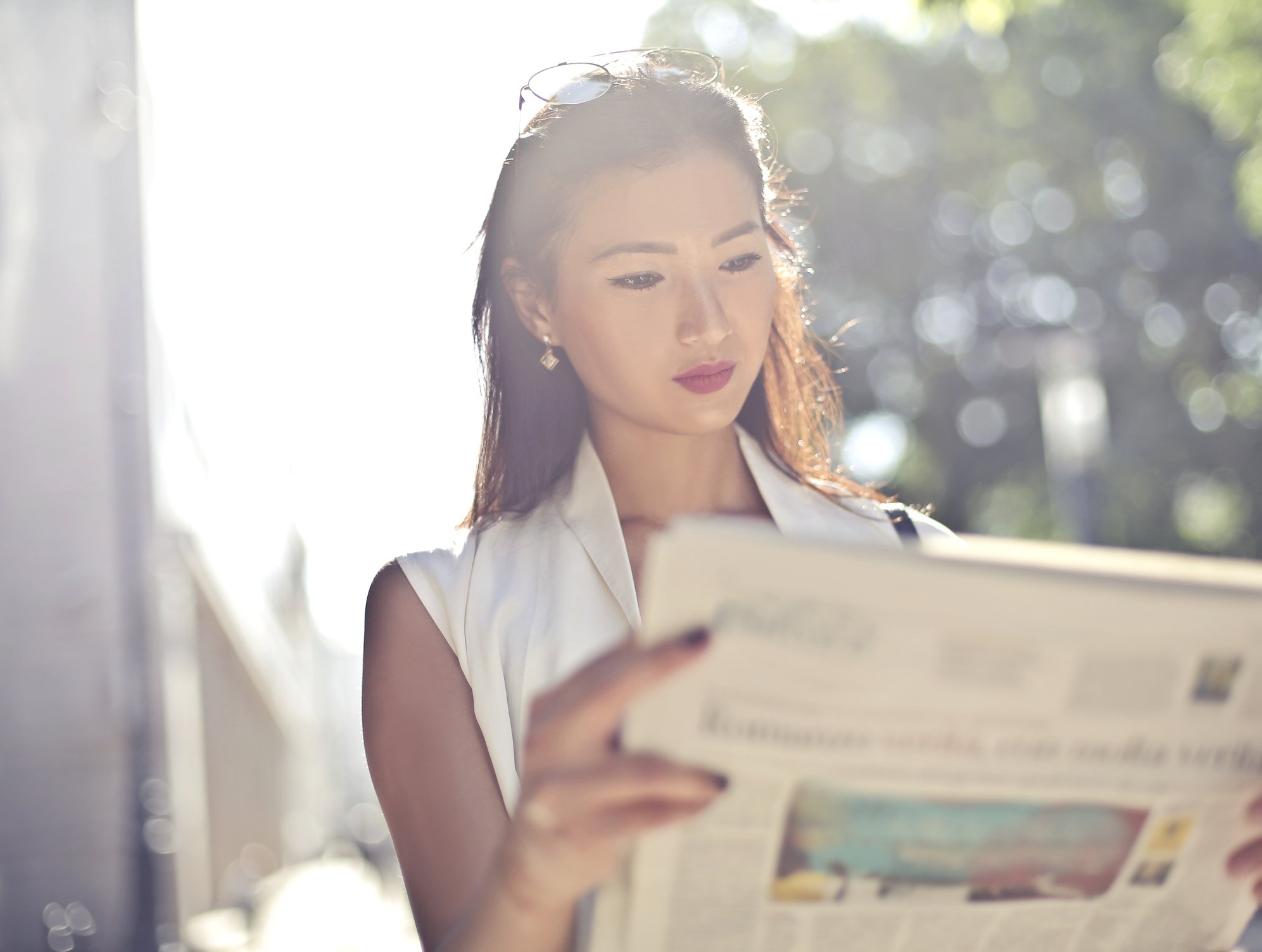 A young woman reads a newspaper.