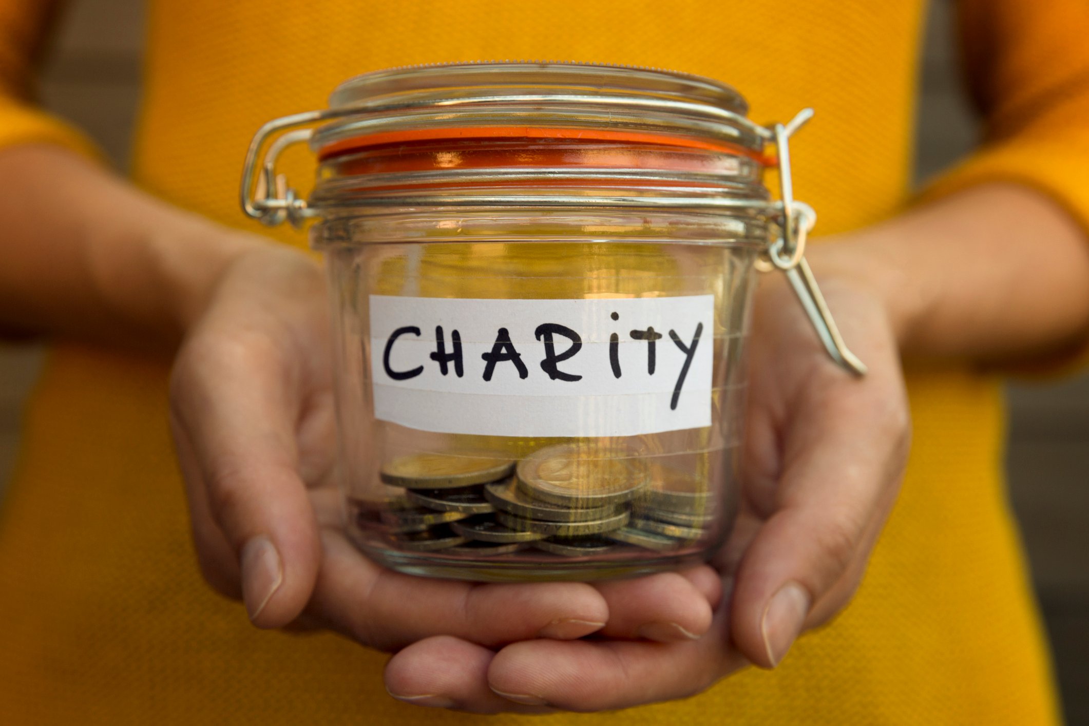 A person holds a jar with coins in it  that says charity