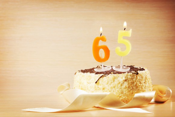 Cake with lit candles in the shape of the numbers 6 and 5 on top.
